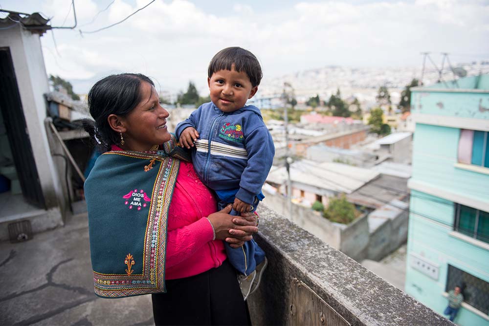 David's mom holds him in her arms with a view of Quito