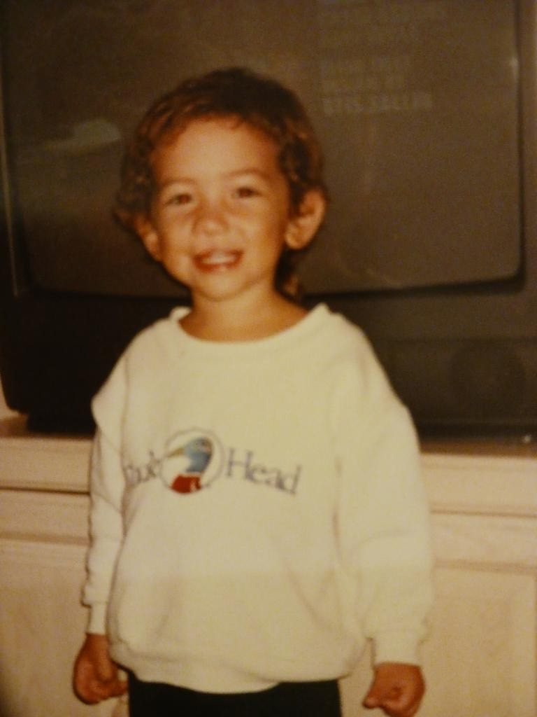 Young Dillon smiling and standing in front of a TV