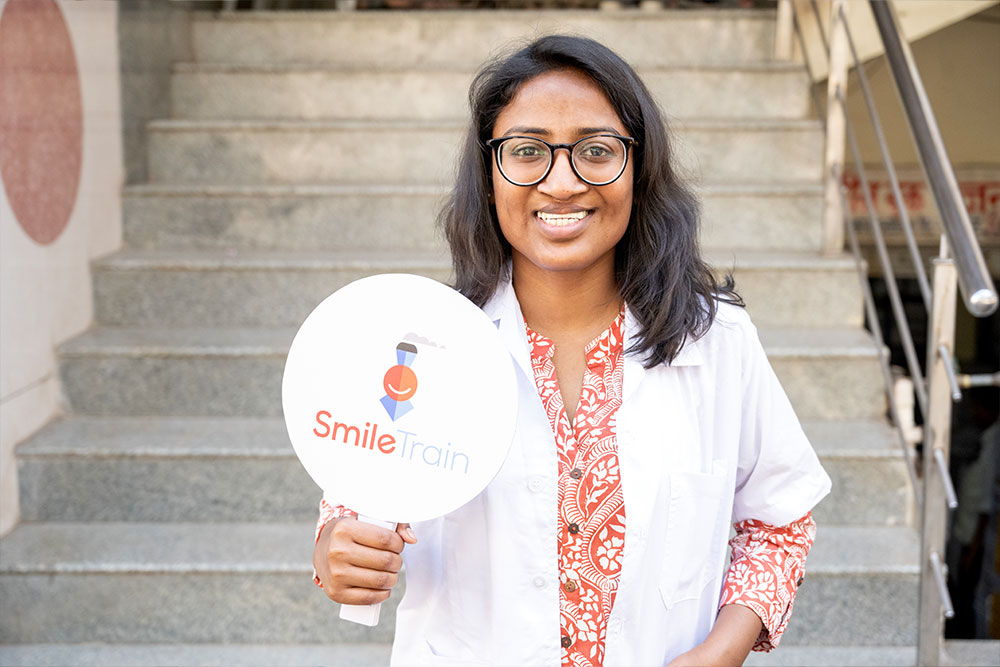 Dr. Mayuri in a lab coat holding a Smile Train sign