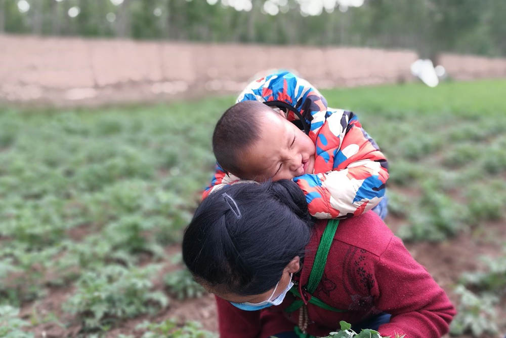 Bao strapped to his mother's back while she works on the farm