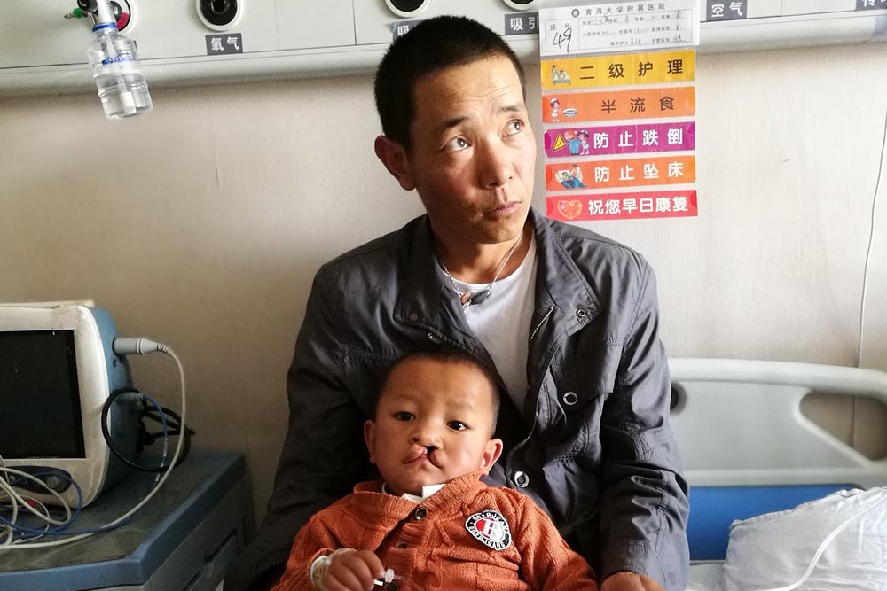 Bao lays on his father's lap in a hospital bed