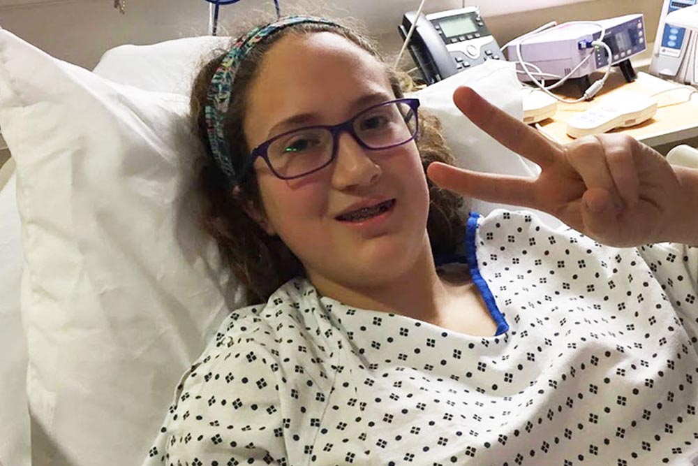 Grace in a hospital bed give peace sign