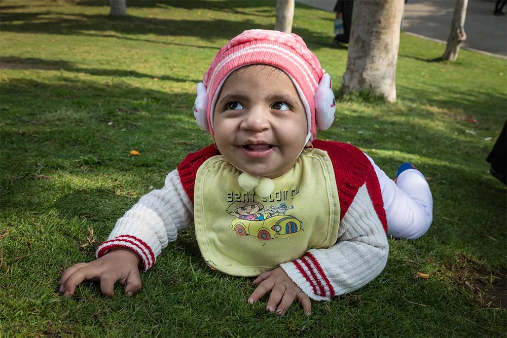 Habeeba crawls on grass with a big smile