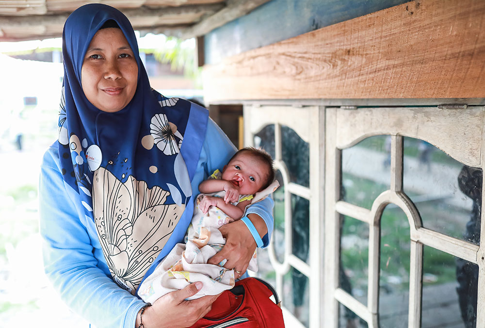 Endang holding a baby with a cleft before their first free cleft surgery
