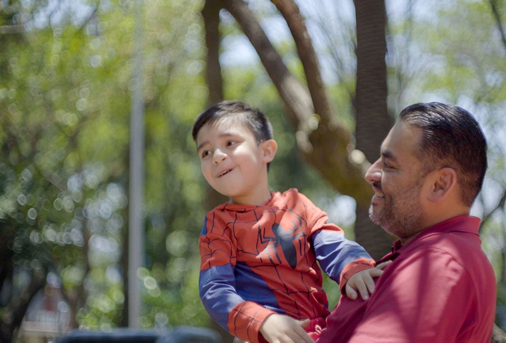 Javier holding Damian, who is dressed like Spider-Man