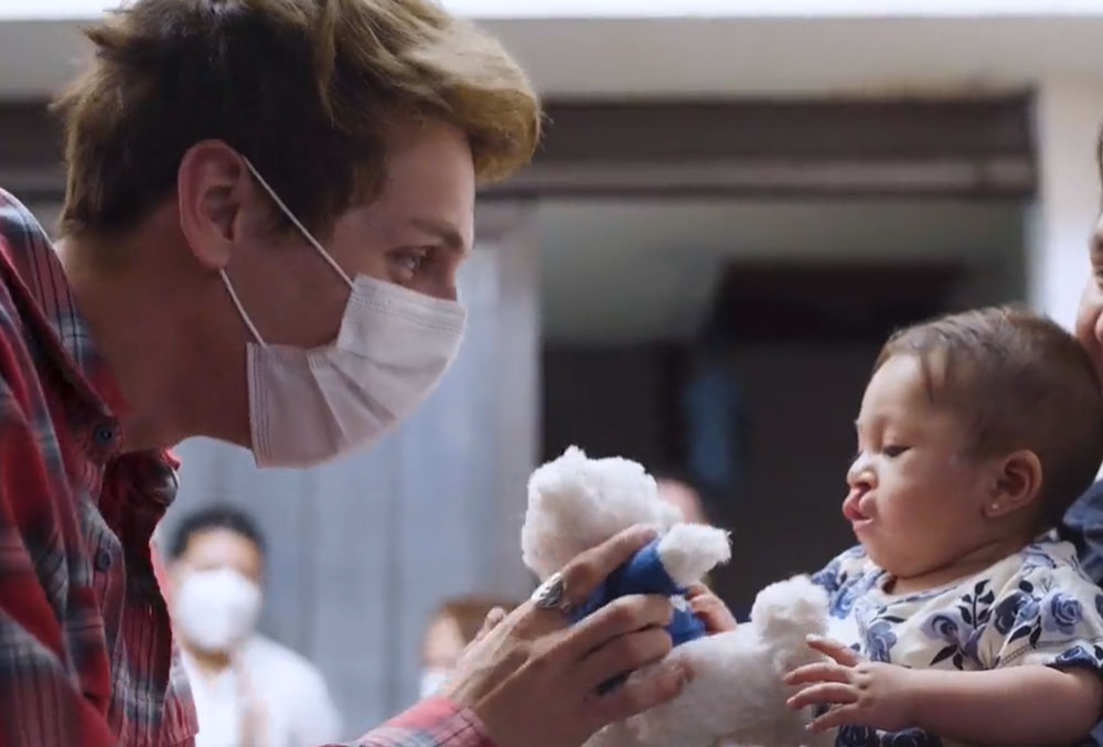 Jacob hands a Smile Train teddy to patient Sugey while visiting her home