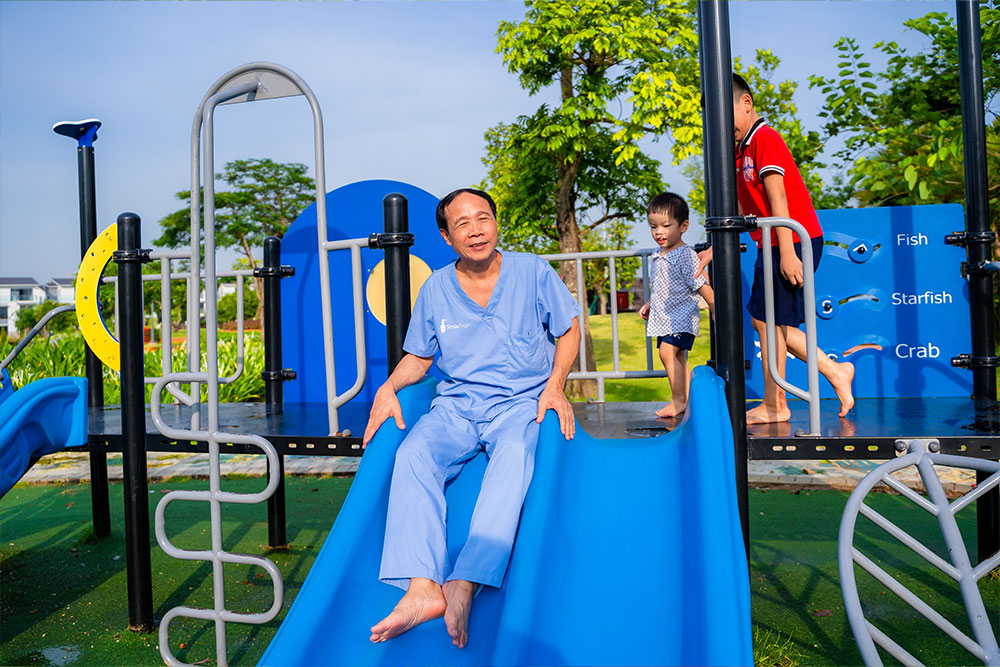Dr. Hoc Trinh going down a slide at a playground with his patients Dat and Quy