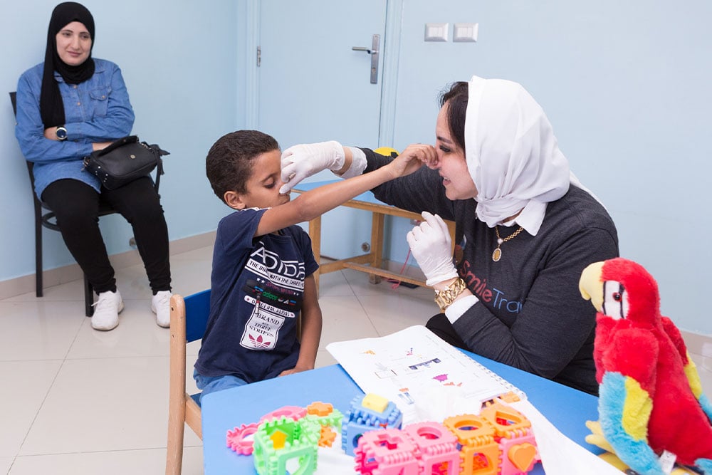 Dr. Sally working with a Smile Train speech patient, holding his nose