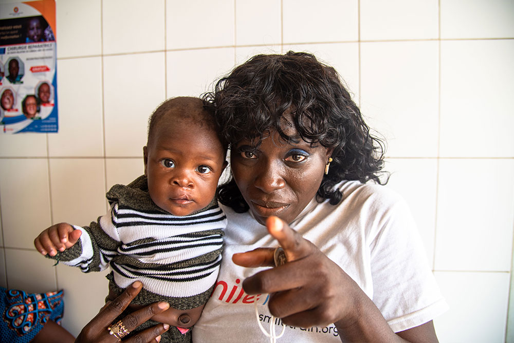 Nina smiling and pointing to the camera with a baby with a cleft after their surgery