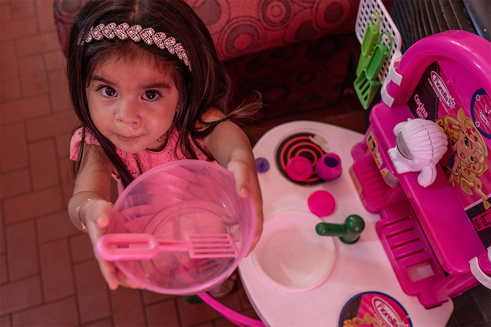 Isabella playing with her toy kitchen, holding up a bowl