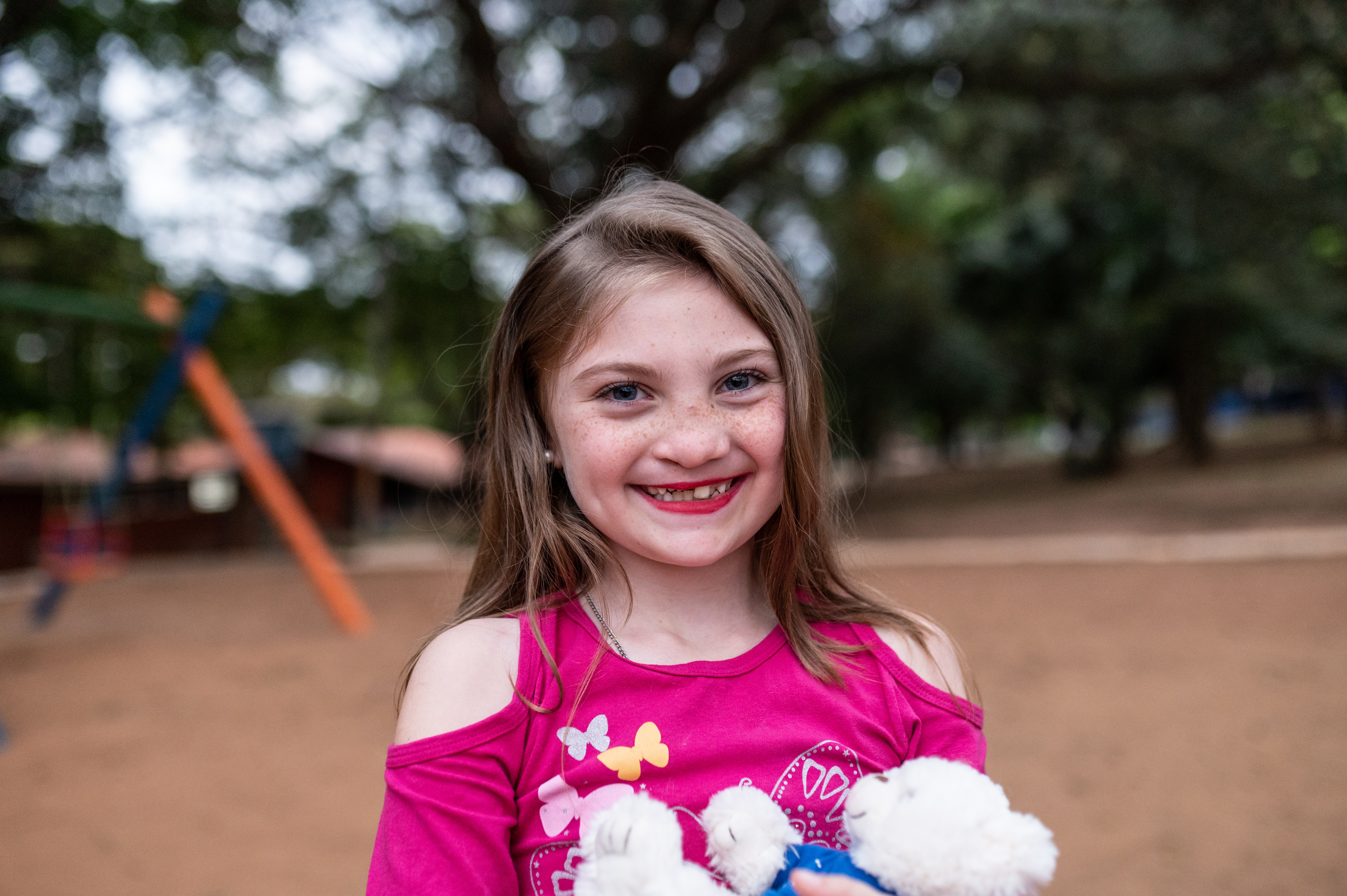 Milena smiling on the playground and holding a white teddy bear