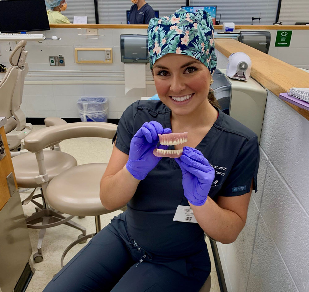 Tammy holding a set of plastic teeth in her chair in dental school