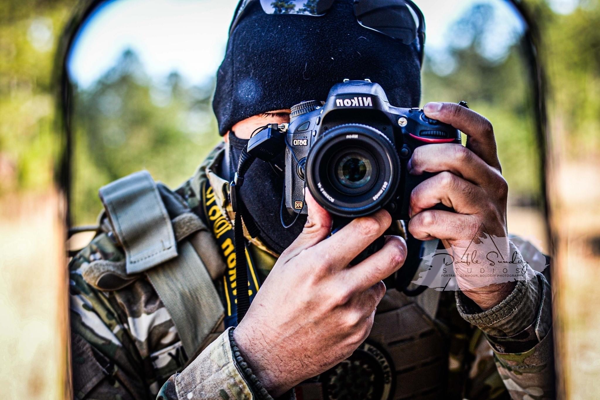 Dillon holding a camera up to his face, taking a picture in a mirror. He’s wearing a black mask and beanie, obscuring his face.