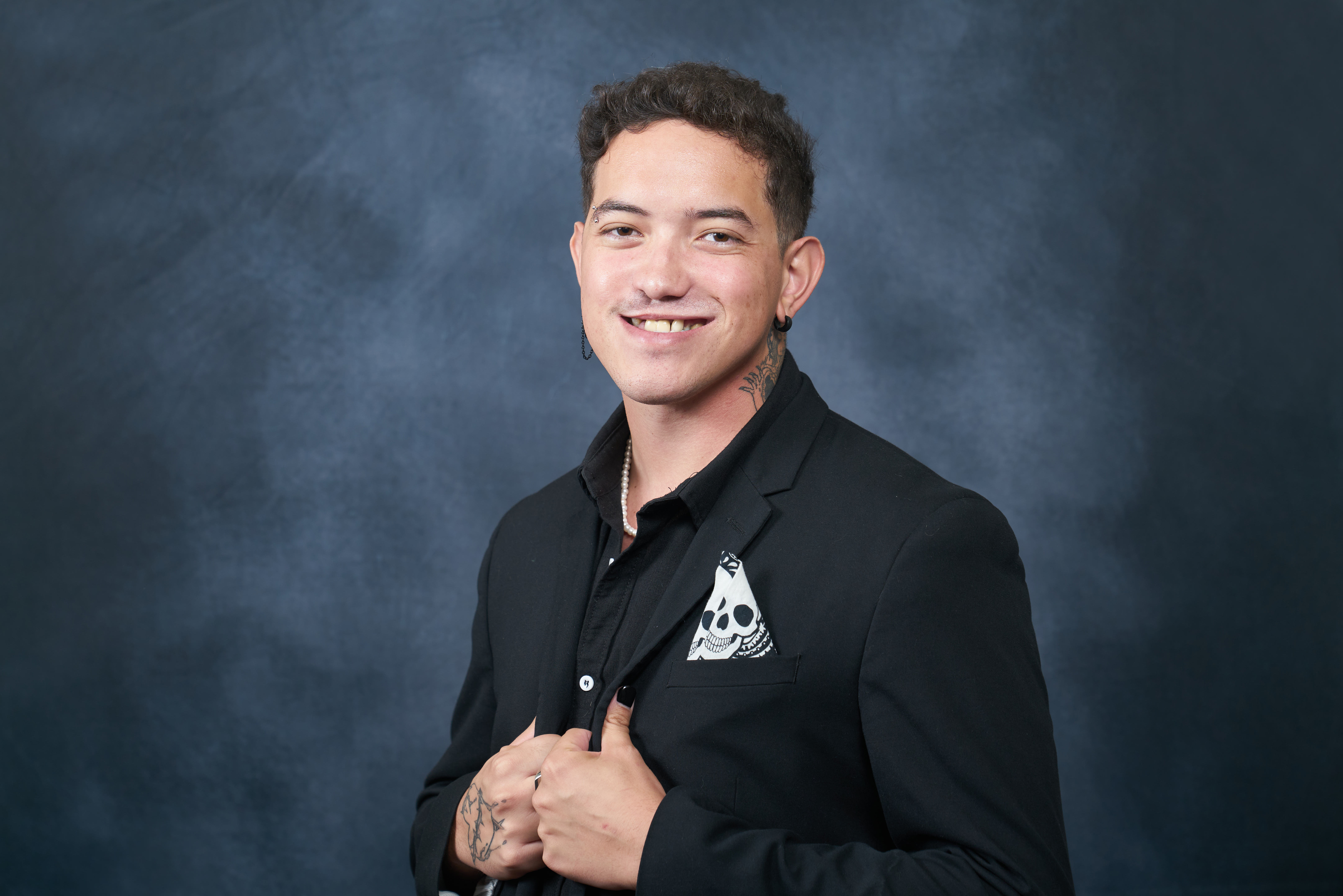A headshot of Dillon wearing a suit on a blue background