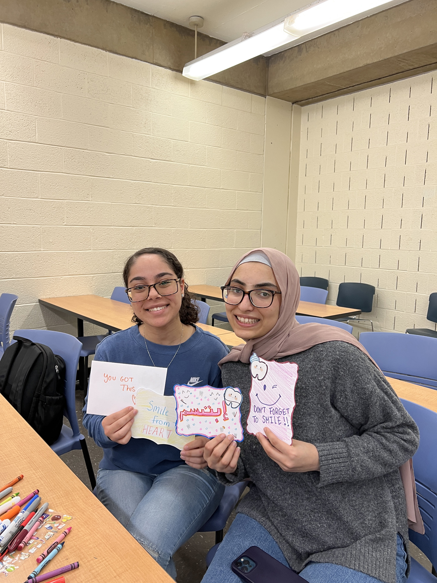 Two Project Dental All members holding up multiple Smile Train cards they’ve made