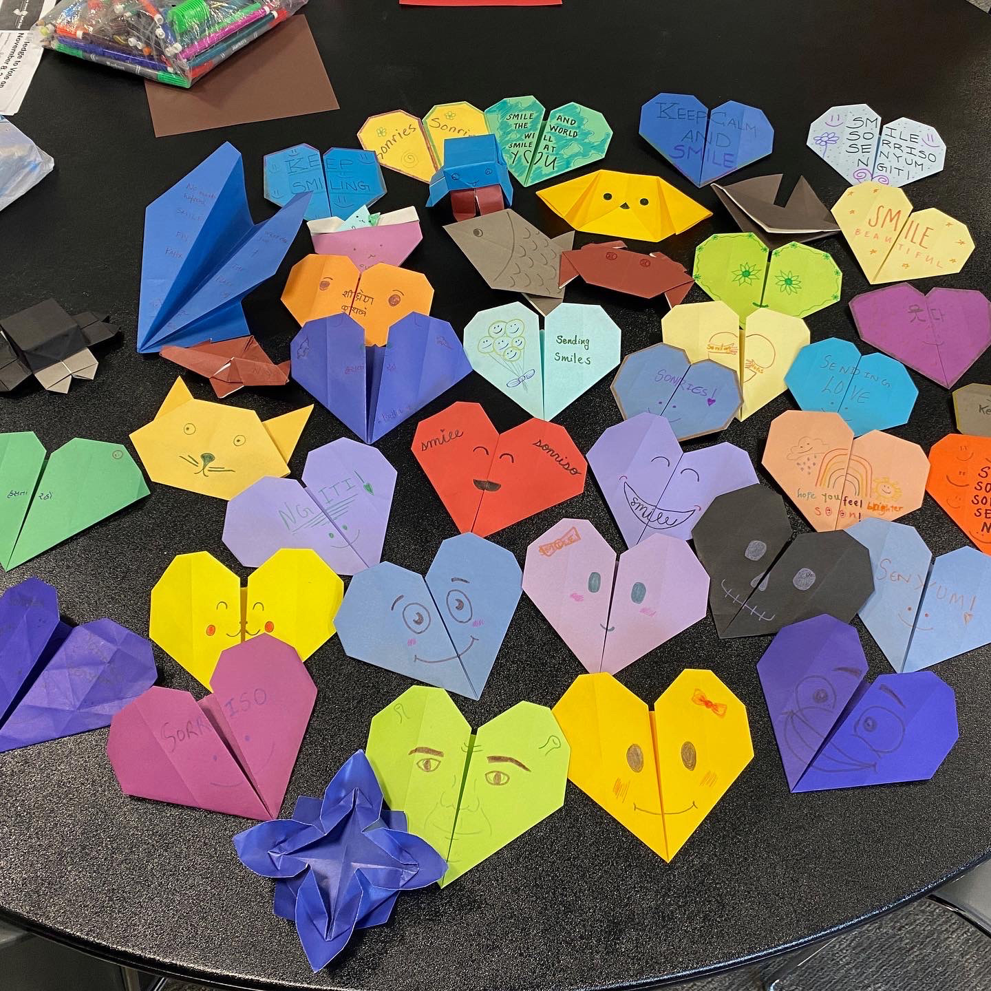 A pile of multicolored heart origami cards with smiles on them