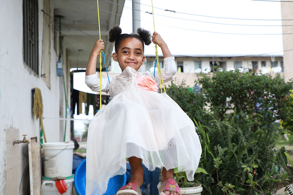 Marsillas smiling, in a while dress standing on a swing