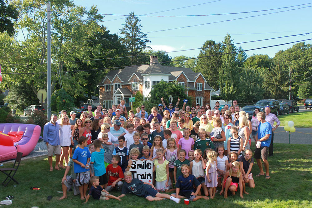 Community engagement: Dozens of Ella’s family and neighbors posing on her lawn at a lemonade stand event