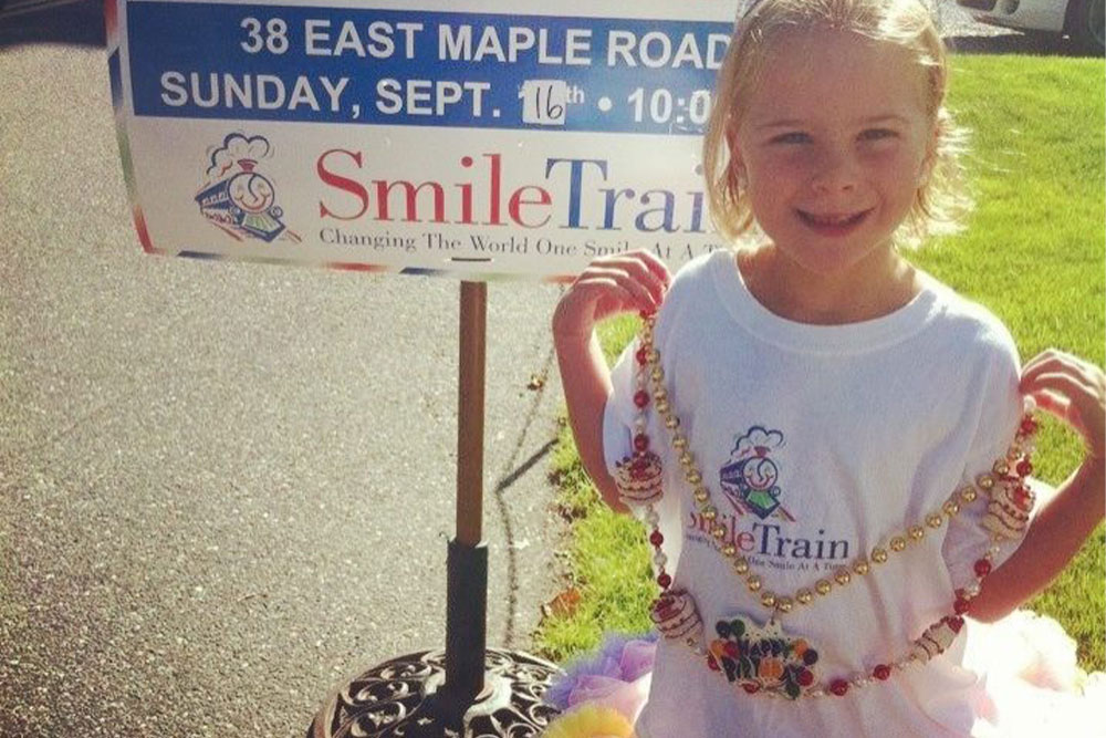 Ella standing in front of a sign promoting her lemonade stand in 2012