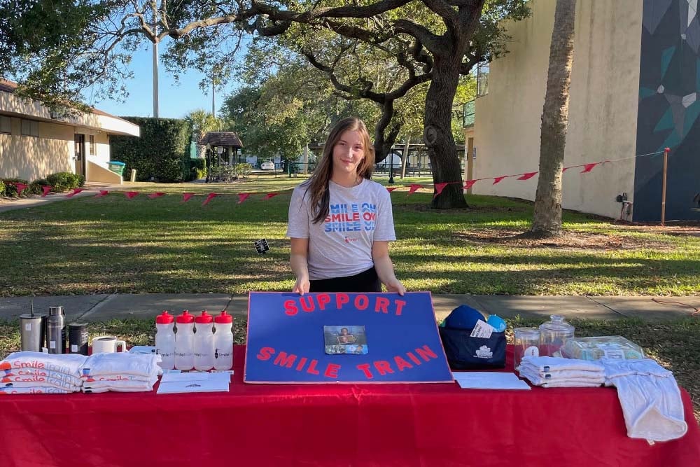 Alexandra standing behind her Smile Train table in front of a field