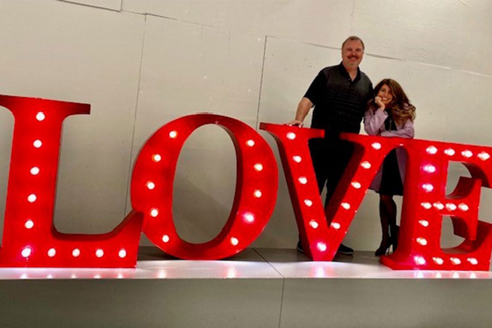 Seth and Becca standing behind a red light-up “LOVE” sign