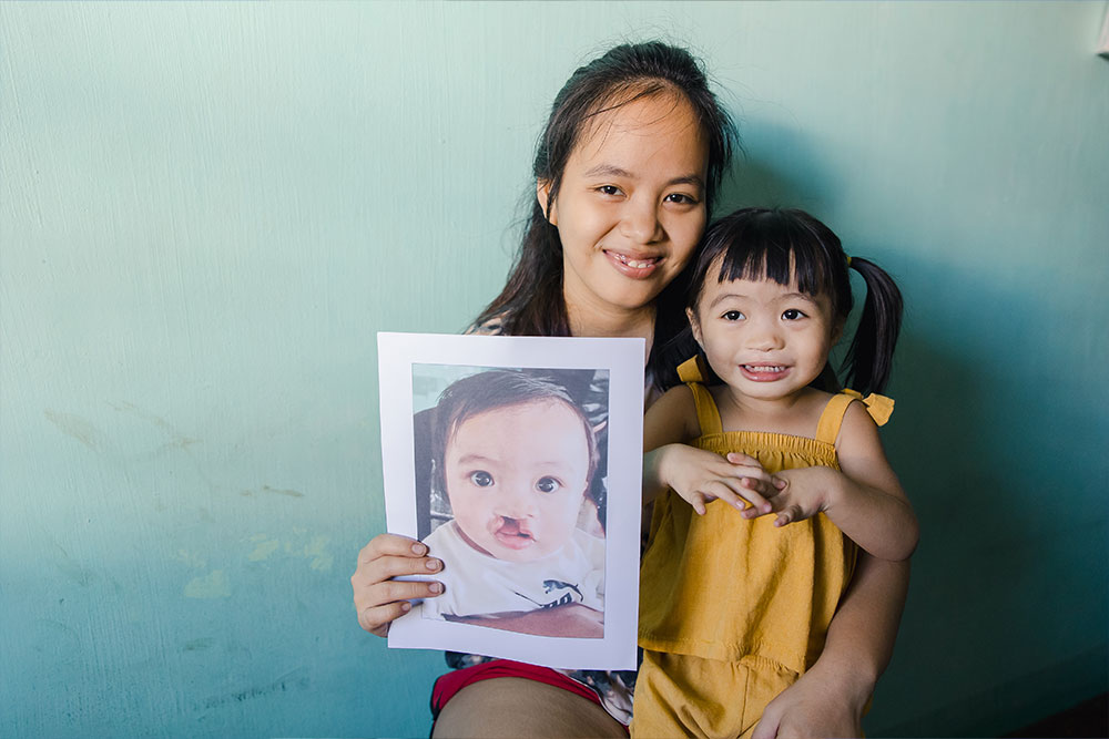 Danna holding Zabriena on her lap and holding a picture of Zabriena before cleft surgery