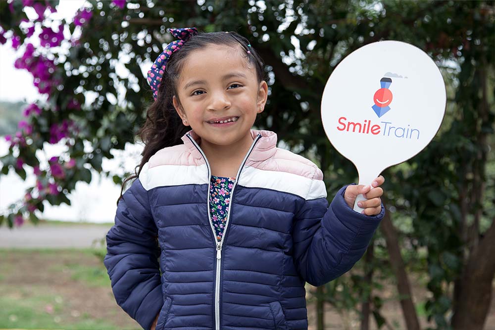 Ivanna smiles and holds up a Smile Train paddle