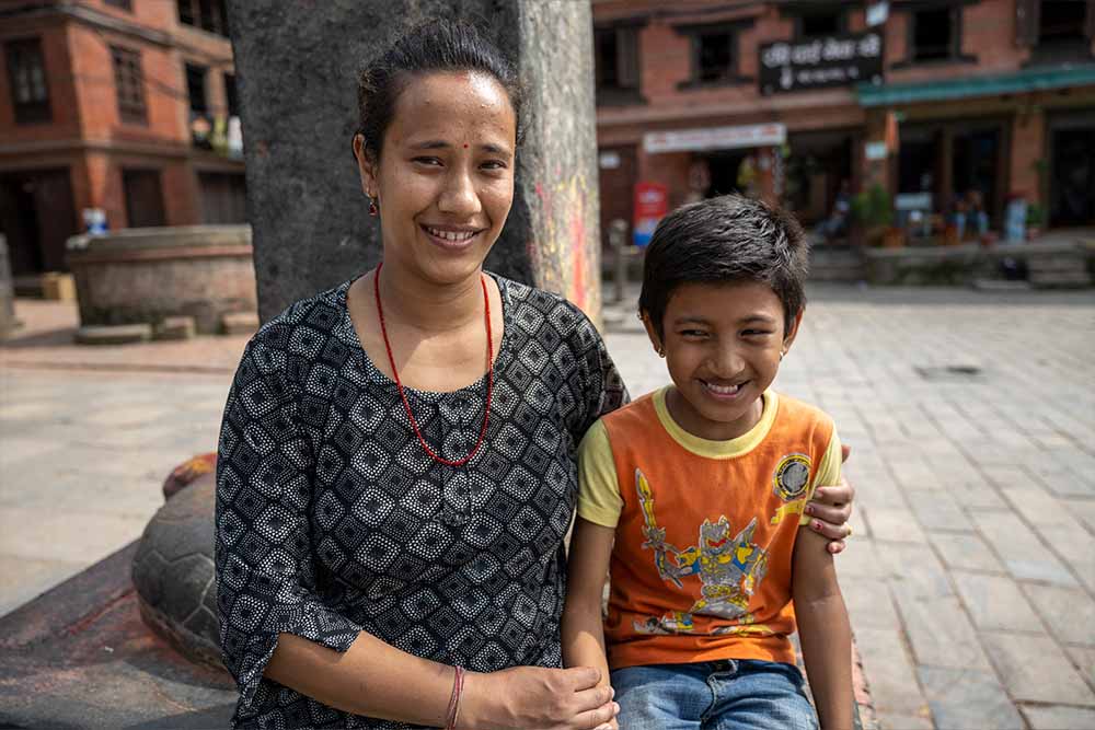 Anjana and Aarosh sit outside and share a smile in the sunlight in their town square
