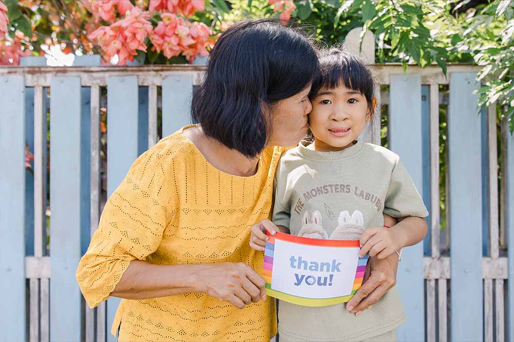Niu's grandmother kisses her and holds a thank you sign after cleft surgery
