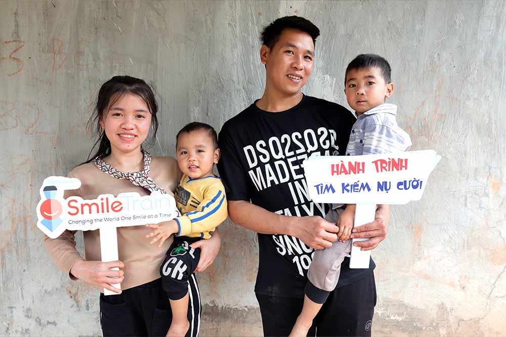 Thuong holds her younger son while her husband holds Gau. They both hold up Smile Train banners