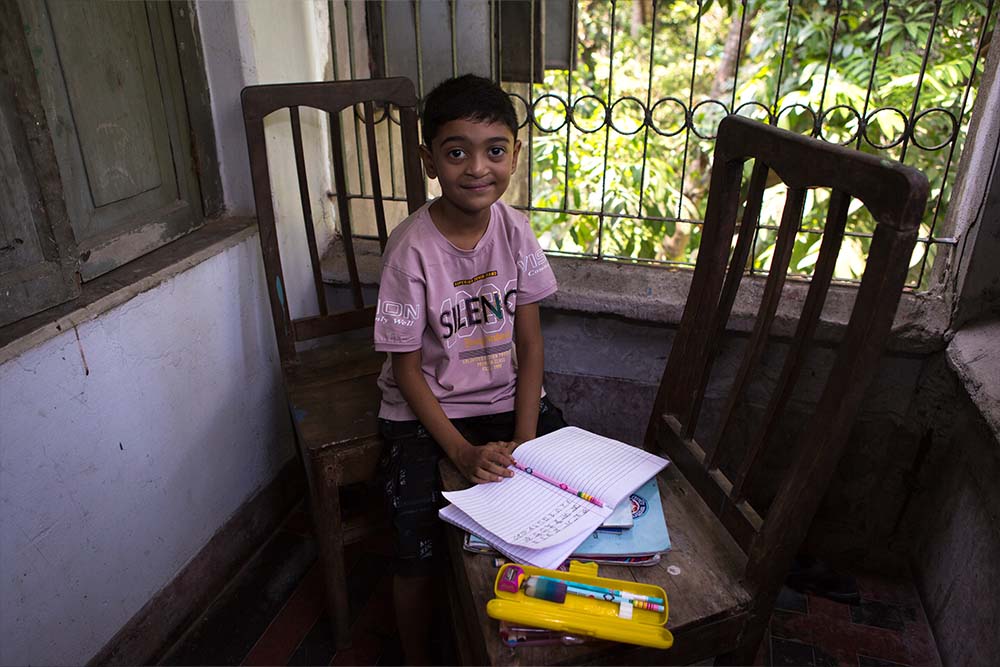 Maimun smiles and sits with his schoolbooks