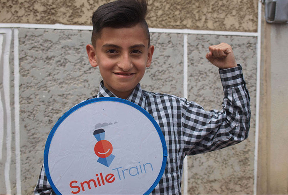 Cristian holding a Smile Train sign and raising a fist in triumph