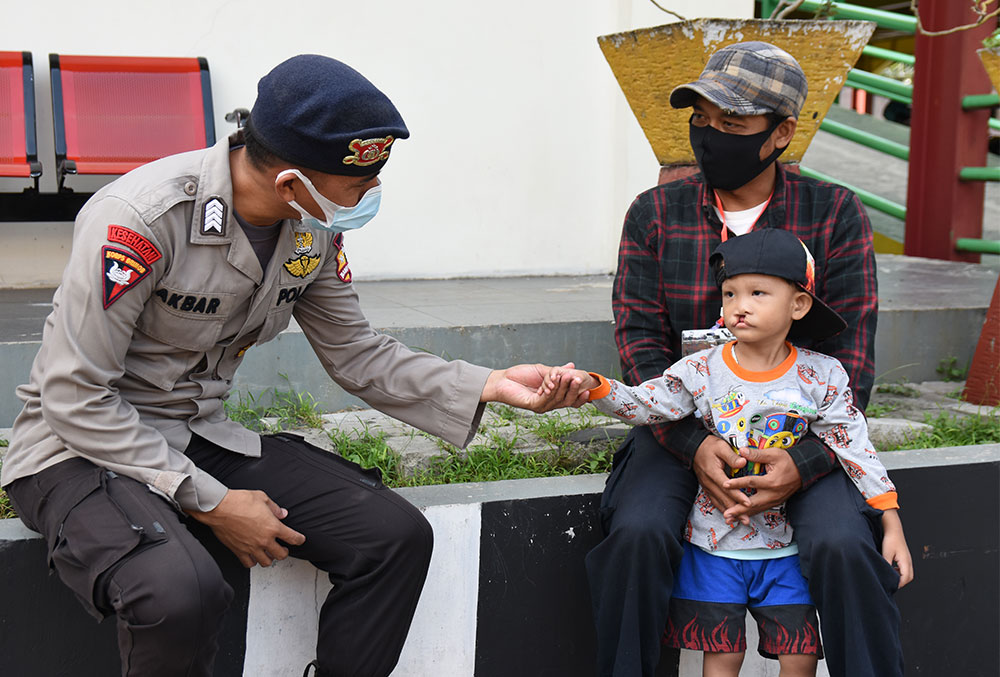 Indonesian police officer reaches out to a boy with a cleft before his free Smile Train surgery