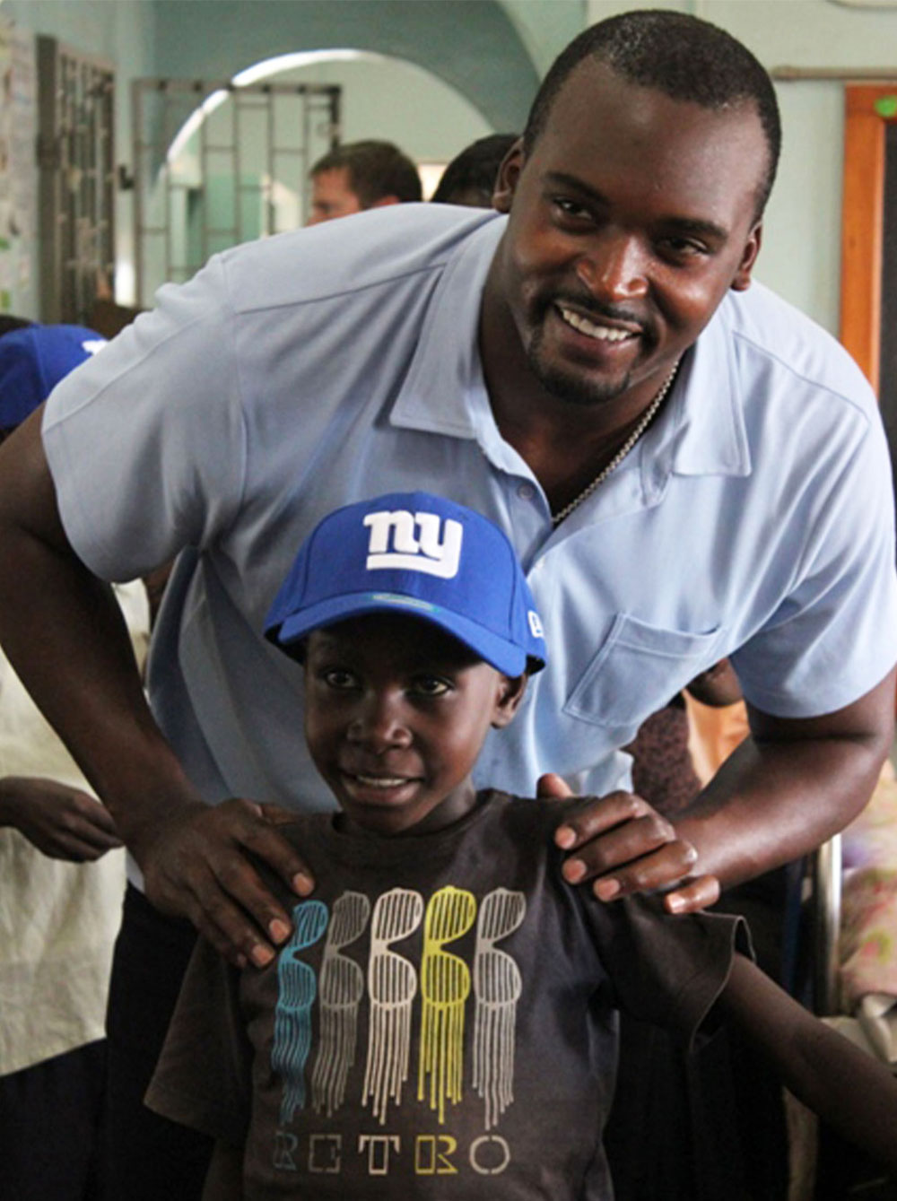 Mathias Kiwanuka in Uganda with a child in a NY Giants hat