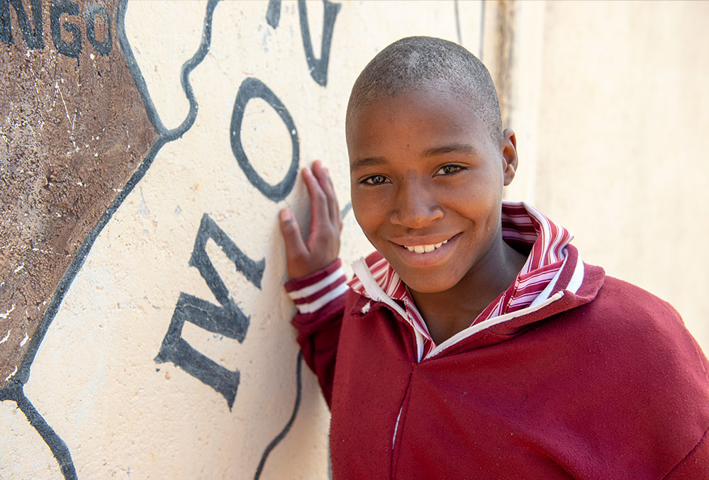 Munashe leans against a map of southern Africa after Smile Train-sponsored cleft surgery