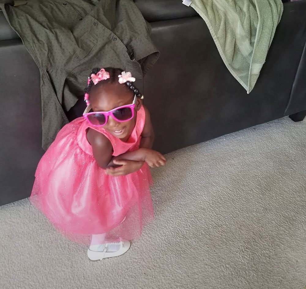 Norah wearing big sunglasses and playfully hides behind a couch