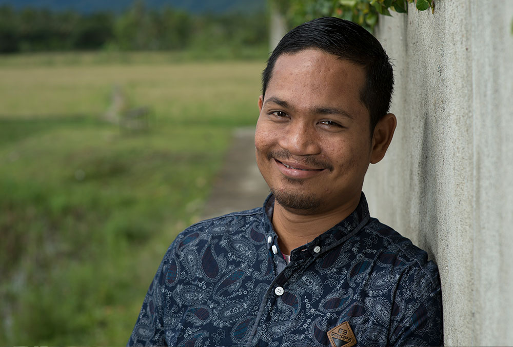 Rahmad leans against a wall while smiling