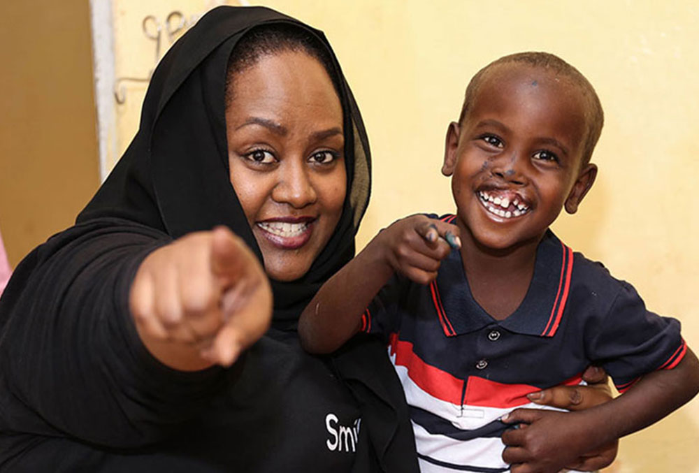 Sesnie pointing to the camera with a Smile Train cleft lip and cleft palate patient