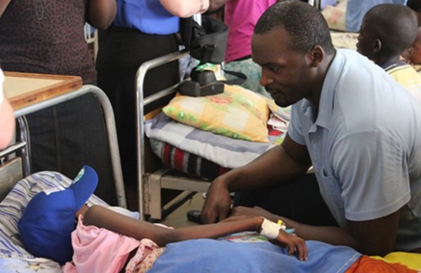 https://www.smiletrain.org/sites/default/files/styles/1_column_470_x_305/public/2021-04/mathias-kiwanuka-in-uganda-with-child-in-bed-ny-giants-hat-cleft-surgery.jpg?itok=Dxia187H