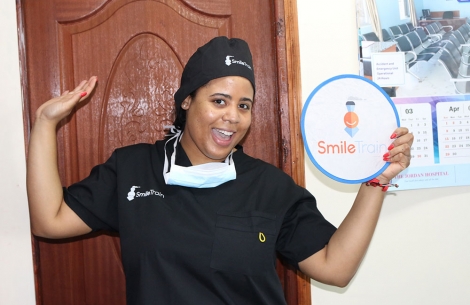 Nijha Diggs wearing scrubs and holding a Smile Train sign before observing a free cleft surgery.