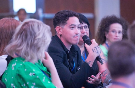 Dillon talking into a microphone at a conference with people surrounding him blurred in the foreground and background