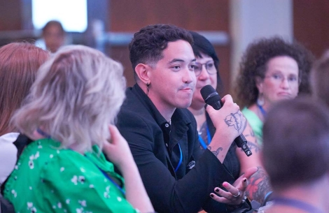 Dillon talking into a microphone at a conference with people surrounding him blurred in the foreground and background