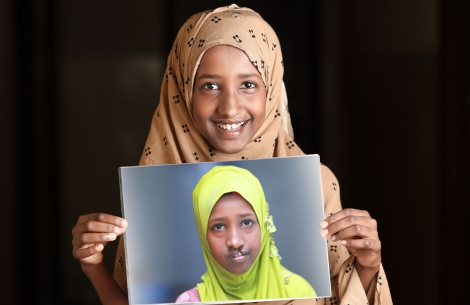 A smiling Maryan holds up a photo of herself from before cleft treatment