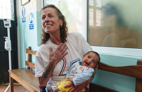 Karen Chambers holding a baby with a cleft with one arm, and her hand over her heart with emotion with the other