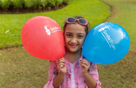 Durva smiles and holds up two Smile Train balloons
