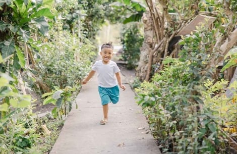 Emmanuel smiles and runs down a path surrounded by lush green plants