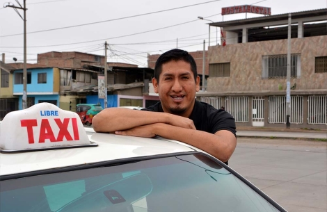 Claudio Chuqui smiles for the camera and rests his arms on top of his taxi cab