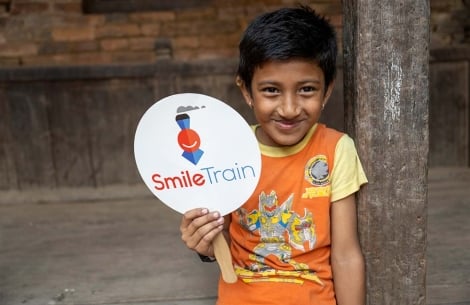 Aarosh grins and holds up a Smile Train paddle logo
