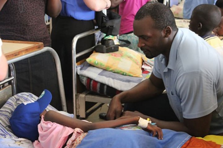 Mathias Kiwanuka visits a child in Uganda wearing a New York Giants hat.