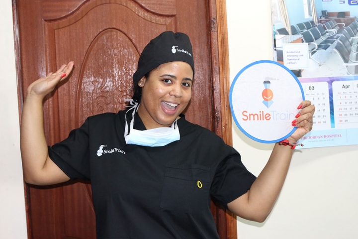 Nijha Diggs wearing scrubs and holding a Smile Train sign before observing a free cleft surgery.